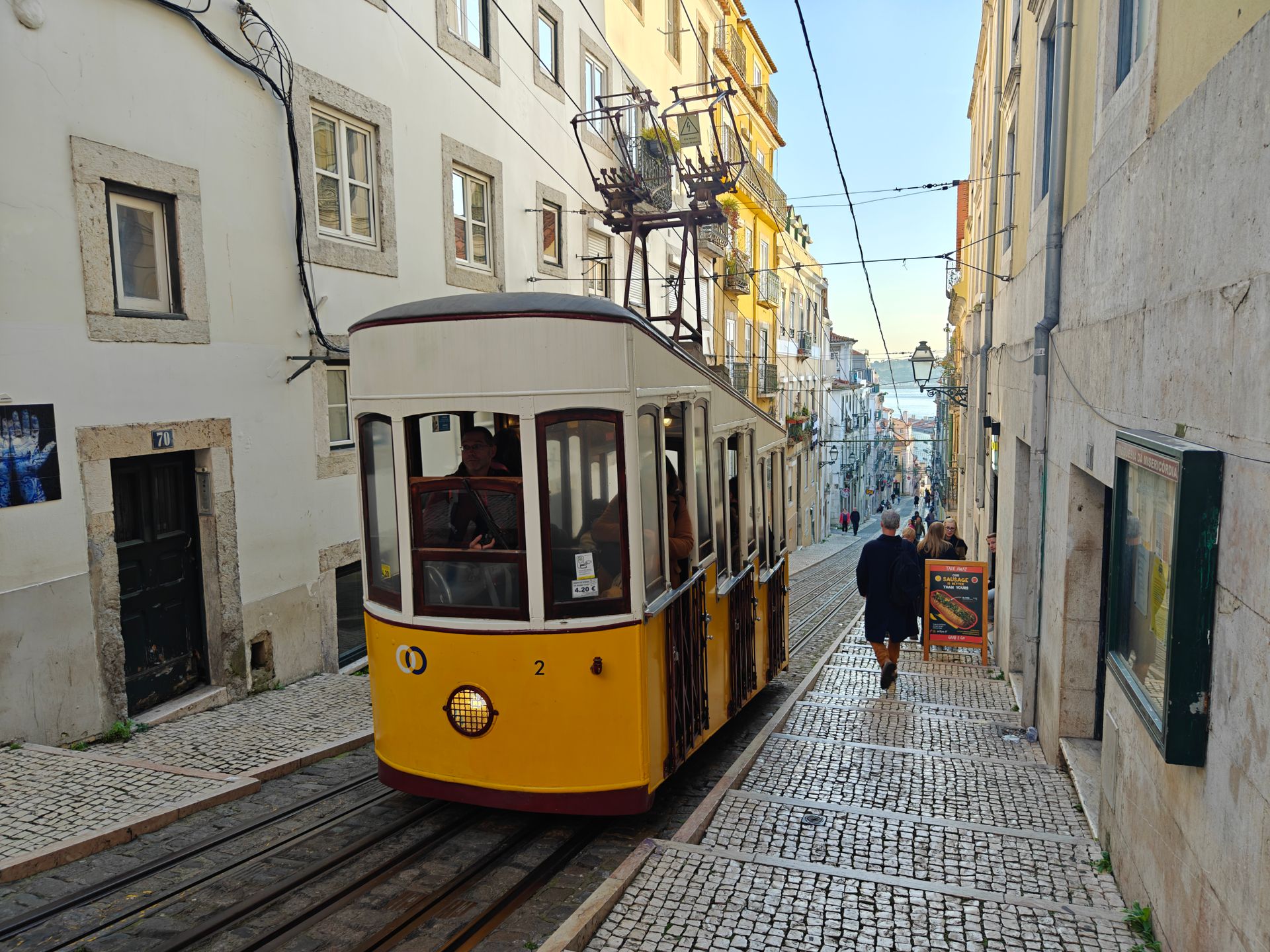 Lisbon's iconic yellow funicular climbing a cobbled street toward the Tagus